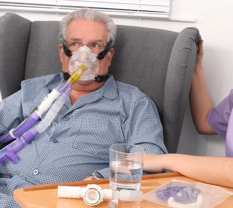 A man sitting in a chair with a breathing mask, showing CPAP breathing circuits by Armstrong Medical